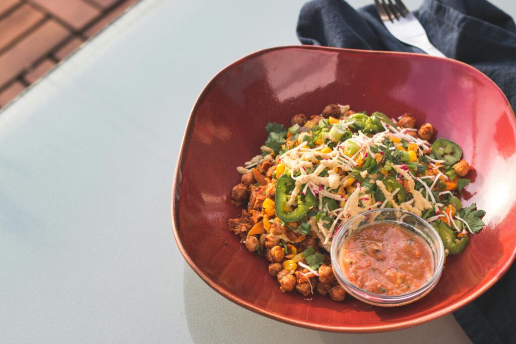 A vibrant chickpea salad served with salsa in a red bowl on a glass table.